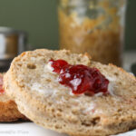 a sliced half of a wholegrain english muffin with melted butter and jam on a white plate