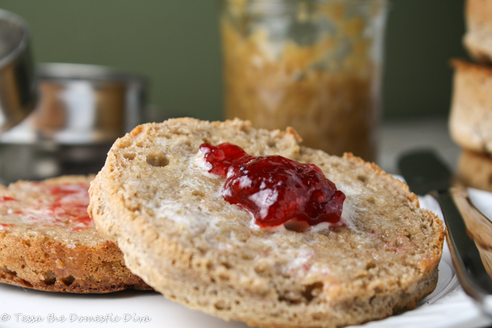 a sliced half of a wholegrain english muffin with melted butter and jam on a white plate