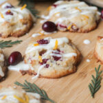 fresh cranberry studded almond cookies with orange zest and a cream cheese glaze on a bamboo cutting surface