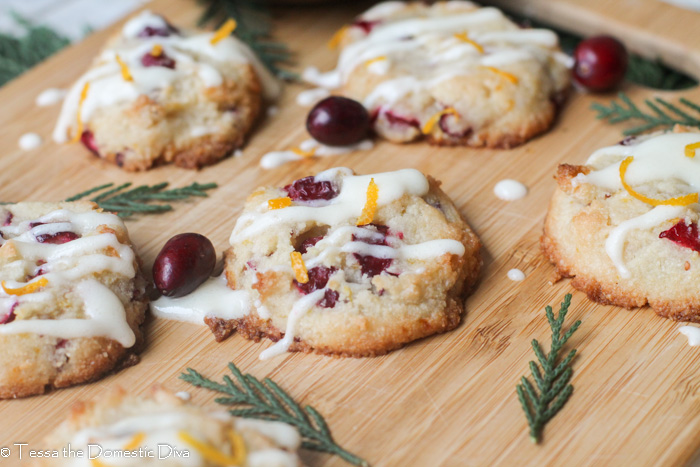 fresh cranberry studded almond cookies with orange zest and a cream cheese glaze on a bamboo cutting surface