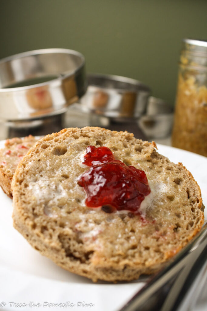 sliced wholegrain english muffin toasted with melted butter and a dollop of jam on a white plate