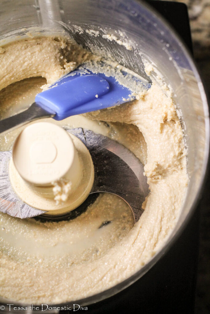 birdseye view of homemade cashew butter inside a food processor bowl with a blue spatula