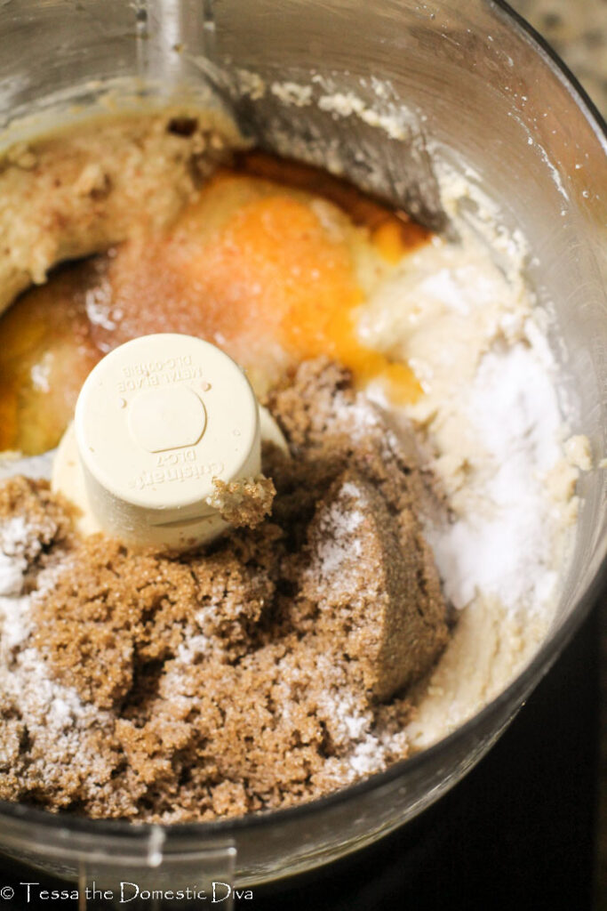 overhead view of a food processor bowl with nut butter, eggs, sugar and baking soda