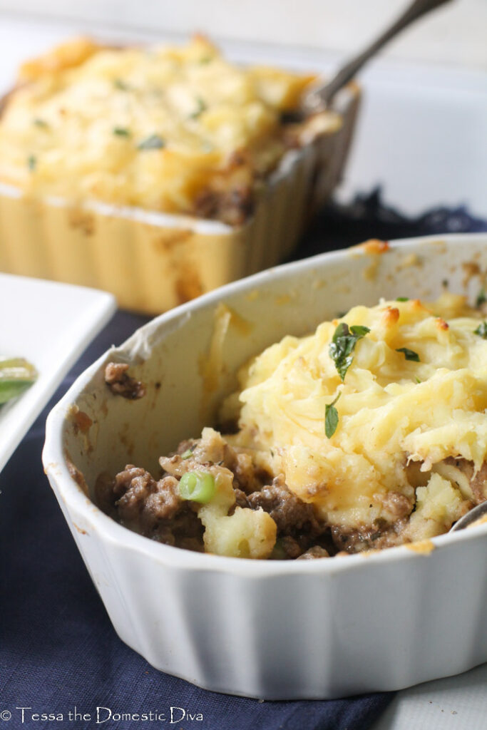 an oval ceraic dish with a cottage pie topped with mashed potato atop a navy blue fabric