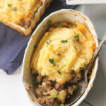 overhead two cermaic dishes filled with cottage pie and a side a green beans