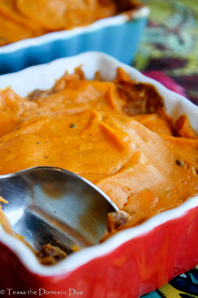 a red and white square ceramic baking dish with aground beef topped with cheesy mashed sweet potatoes