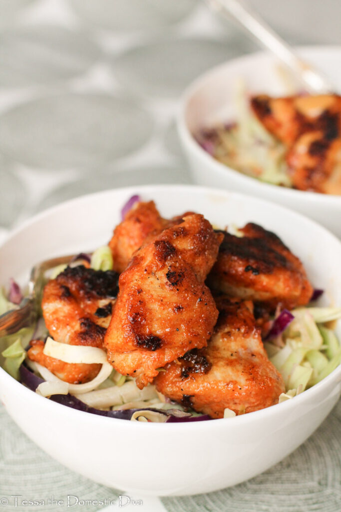 two white bowls filled with Cajun style slaw with zest pan fried chicken breast nuggets