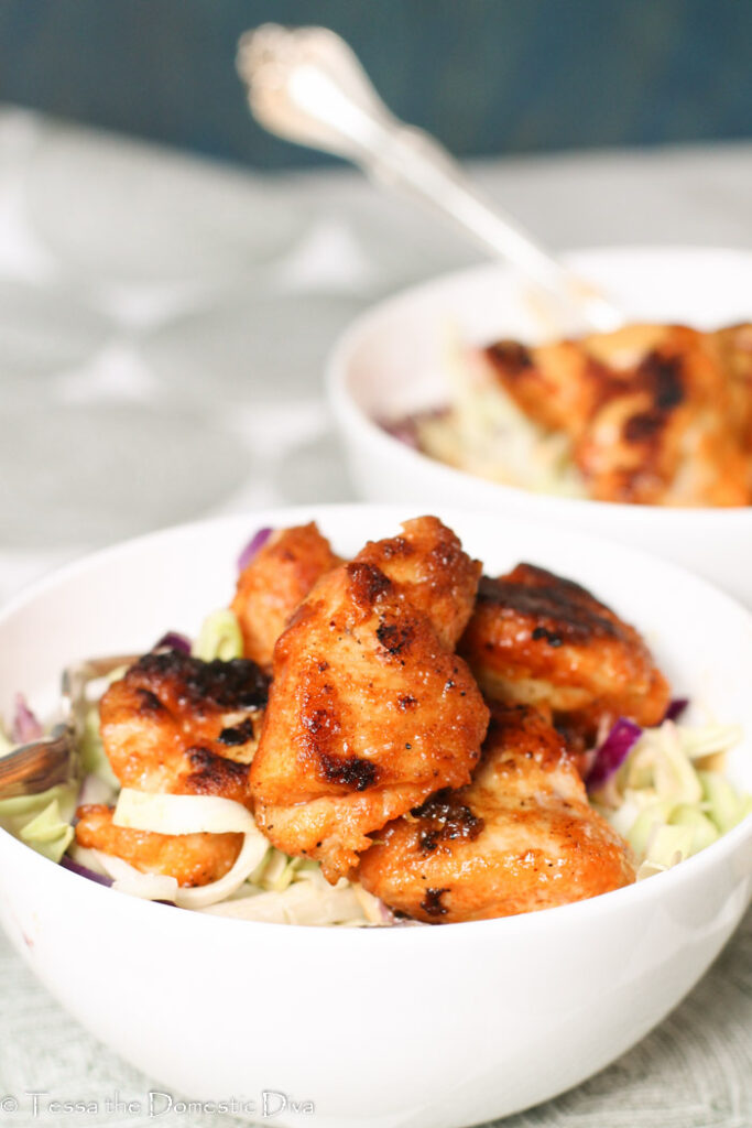 two white bowls filled with a zetsy slaw and pan fried Cajun chicken nuggets