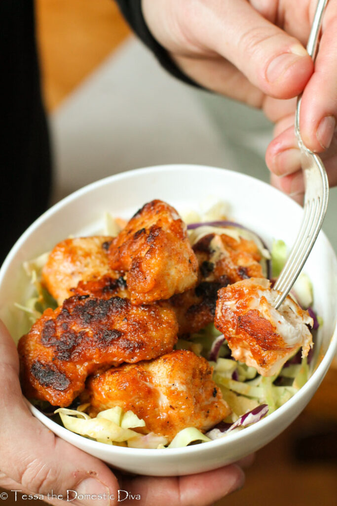 hand held white bowl of Cajun slaw with crispy coated chunks of tender chicken breast coated in a Cajun seasoning