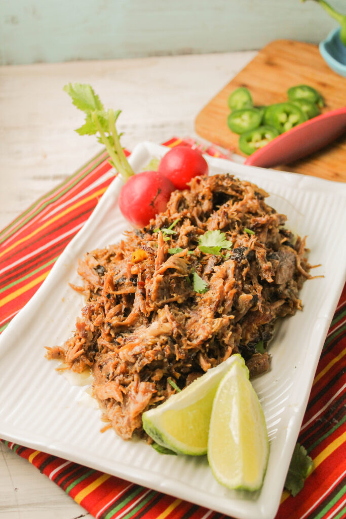 a rectangle white plate with crispy pork carnitas garnished with fresh lime and radishes atop a festive red  striped linen