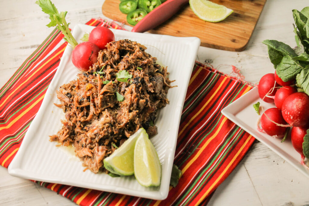 a rectangle white plate topped with crispy pulled pork with cilantro, lime, and radish garnishes