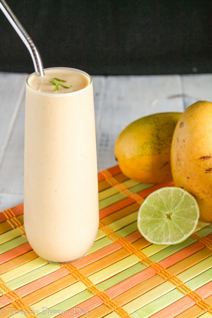 front view of a clearn tall glass with an orange smoothie topped with lime zest and fresh mango