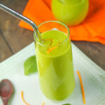 two clear glasses with a creamy green smoothie with fresh orange zest and spinach leaves