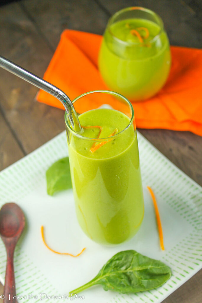 two clear glasses with a creamy green smoothie with fresh orange zest and spinach leaves