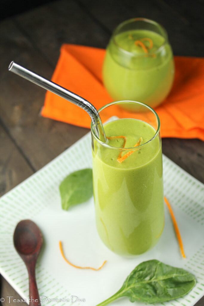 a green orange smoothie in a clear glass with orange zest