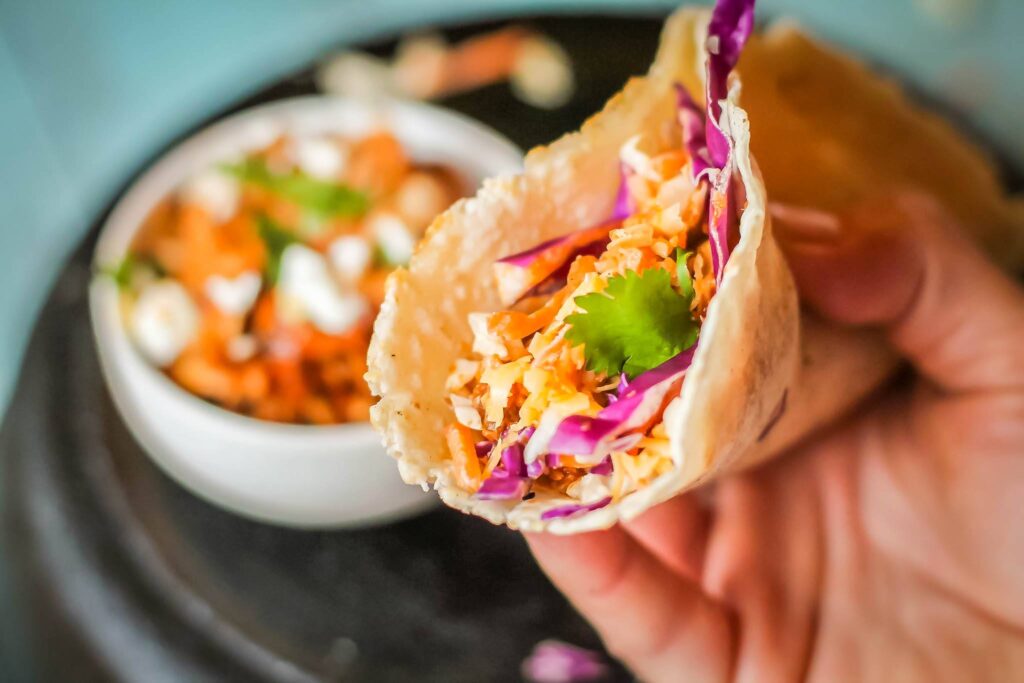 a handheld cassava flour tortillas stuffed with chicken tinga and slaw