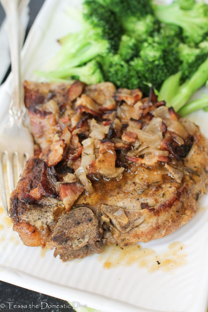 close up view of a single pressure cooker pork chop topped with bacon and gravy.