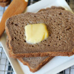two slices of brown bread on a white plate with a pat of butter.
