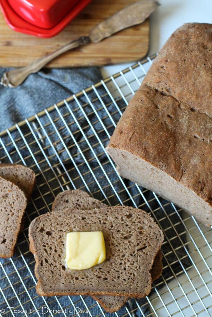 overhead view of a sliced gluten free brown bread on a cooling rack with a square of butter.